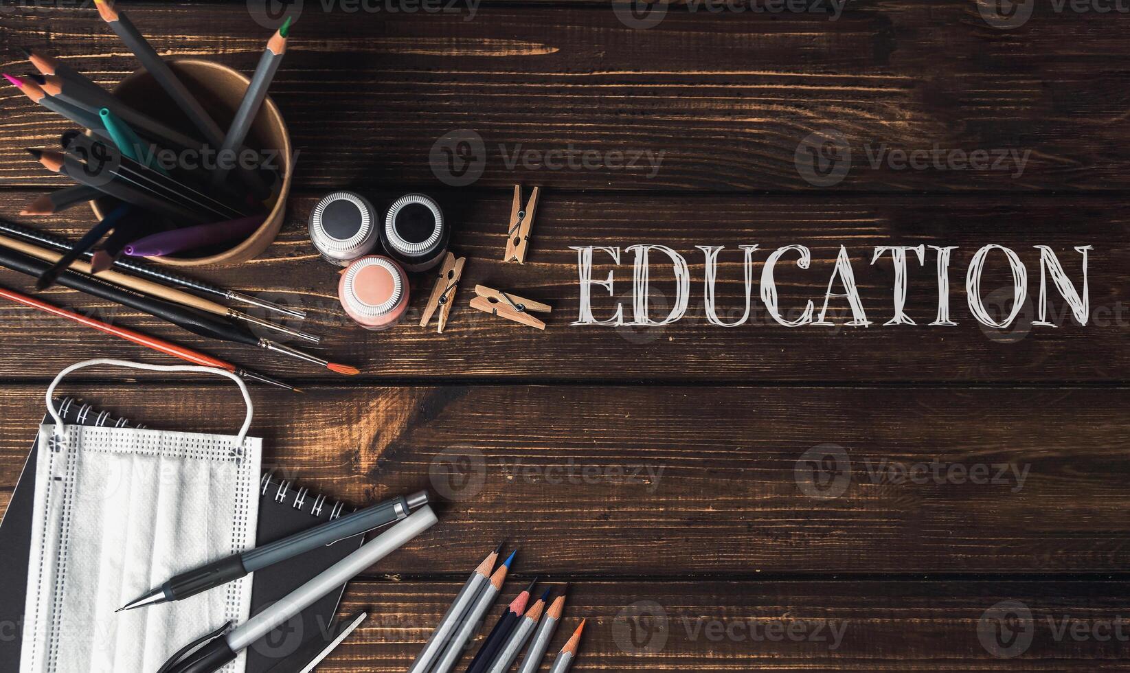 A wooden table with a bowl of pencils, a bottle of paint, and a pair of scissors photo