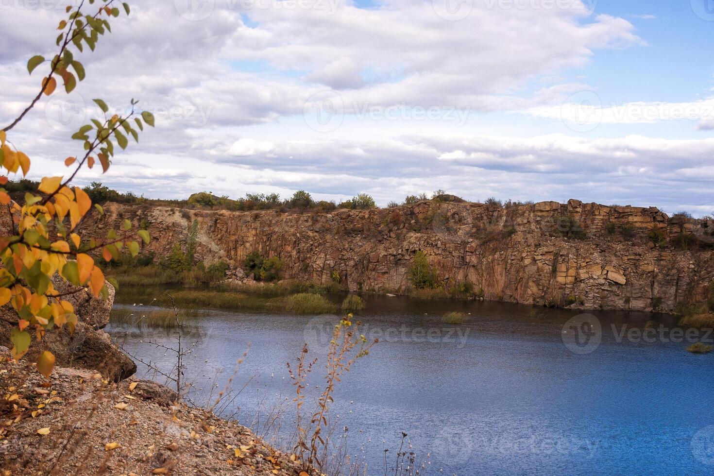fantastic autumn in a mountain canyon. huge granite boulders around a huge bright blue lake. aktovsky canyon in ukraine with cliffs. trees with yellow leaves grow on the tops. photo