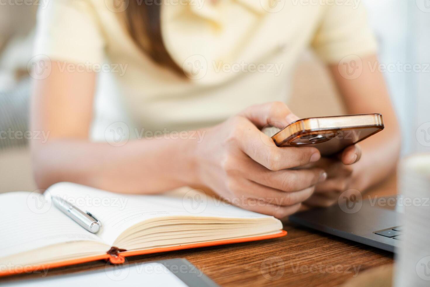Close-up of a woman holding a smartphone, with a notebook and laptop on a wooden desk, creating a cozy work-from-home atmosphere. photo