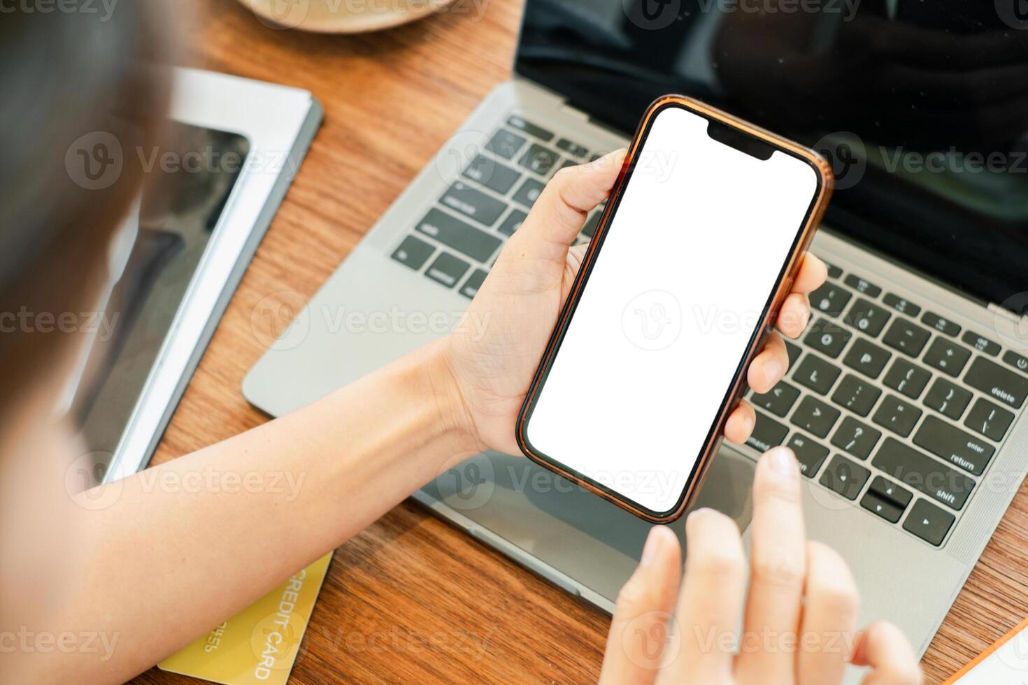 Close-up of hands holding a smartphone with a blank screen above a laptop, ideal for technology or business themes. photo