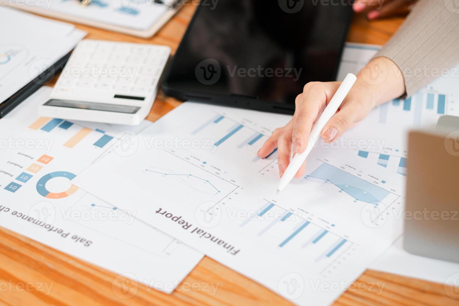 Close-up of a person reviewing financial documents with charts, graphs, calculator, and tablet on a wooden desk. photo