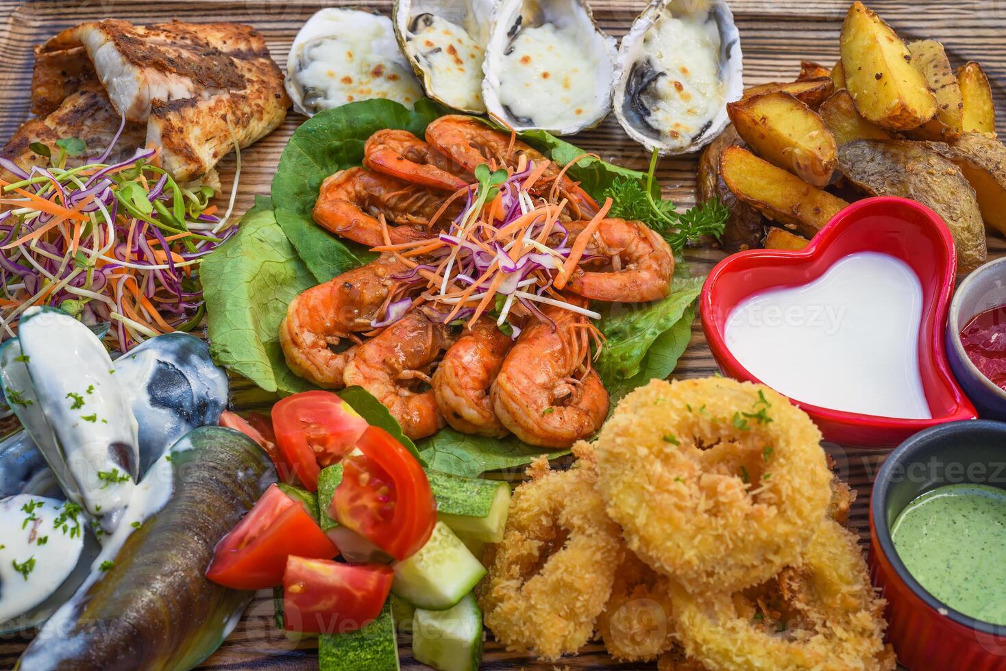 A lot of seafood as fried fish, calamari, oyster and sauce on wooden board on the table photo