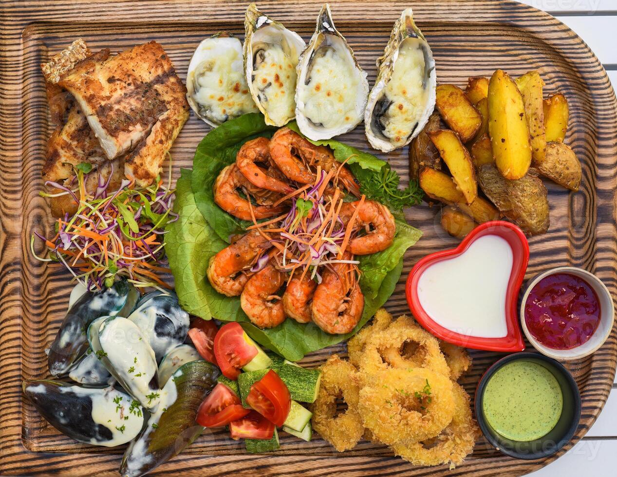 A lot of seafood as fried fish, calamari, oyster and sauces on wooden board on the table photo