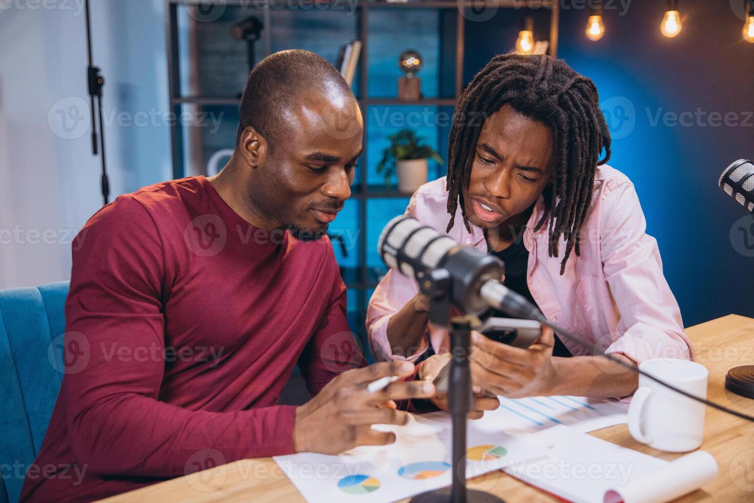 Podcasters reviewing data on smartphone screen, discussing analytics during live recording session with professional microphone photo