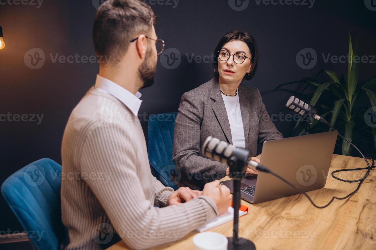 Two content creators recording a podcast in a professional studio, using microphones and a laptop photo