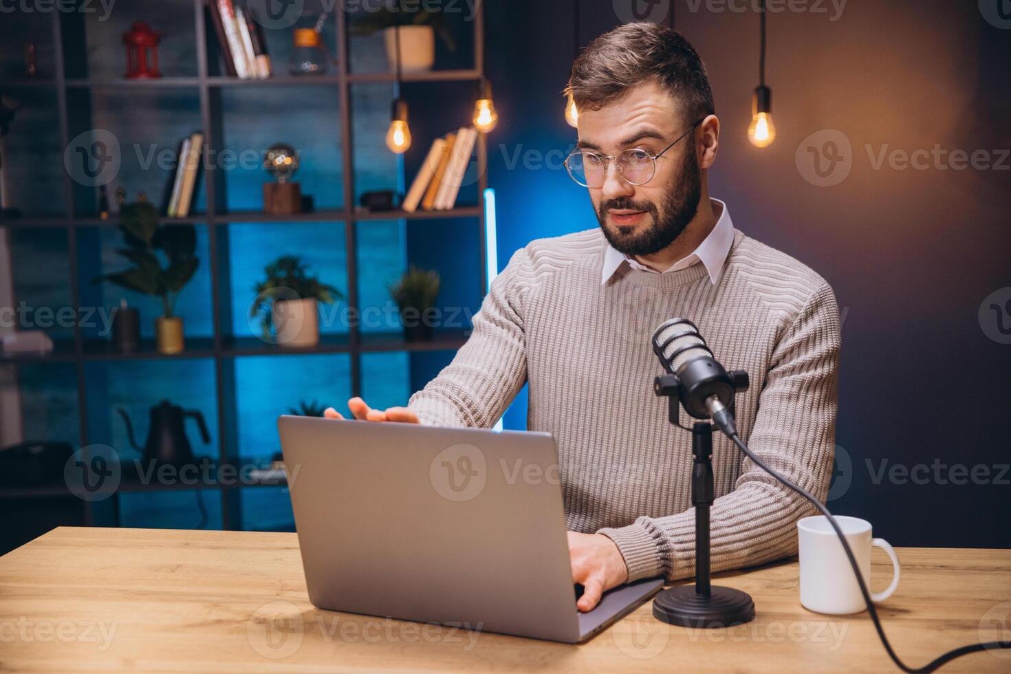Podcaster speaking into condenser microphone while working on laptop in home recording space photo