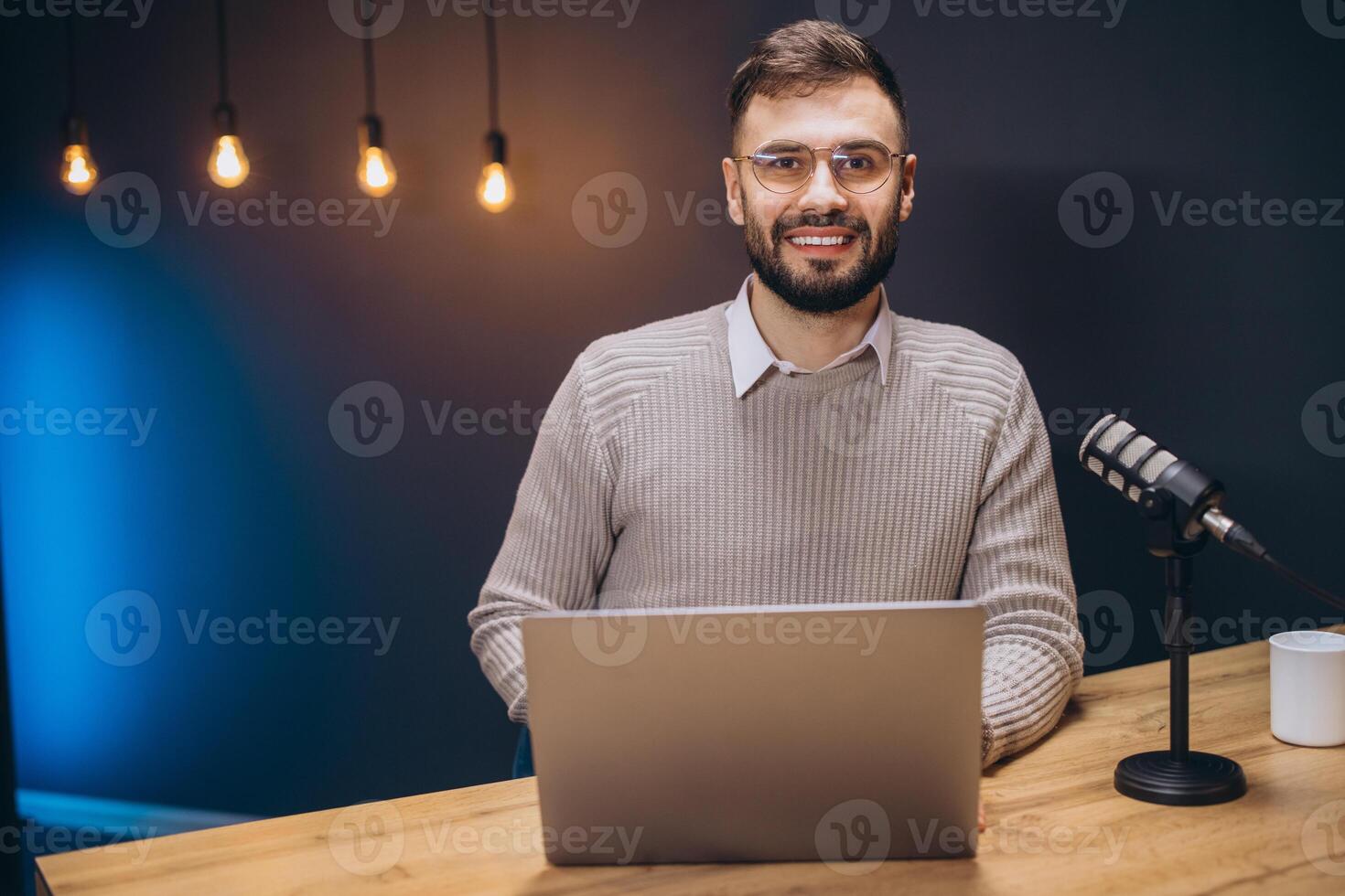 Young podcaster using a laptop and a microphone while recording audio content in a professional studio photo
