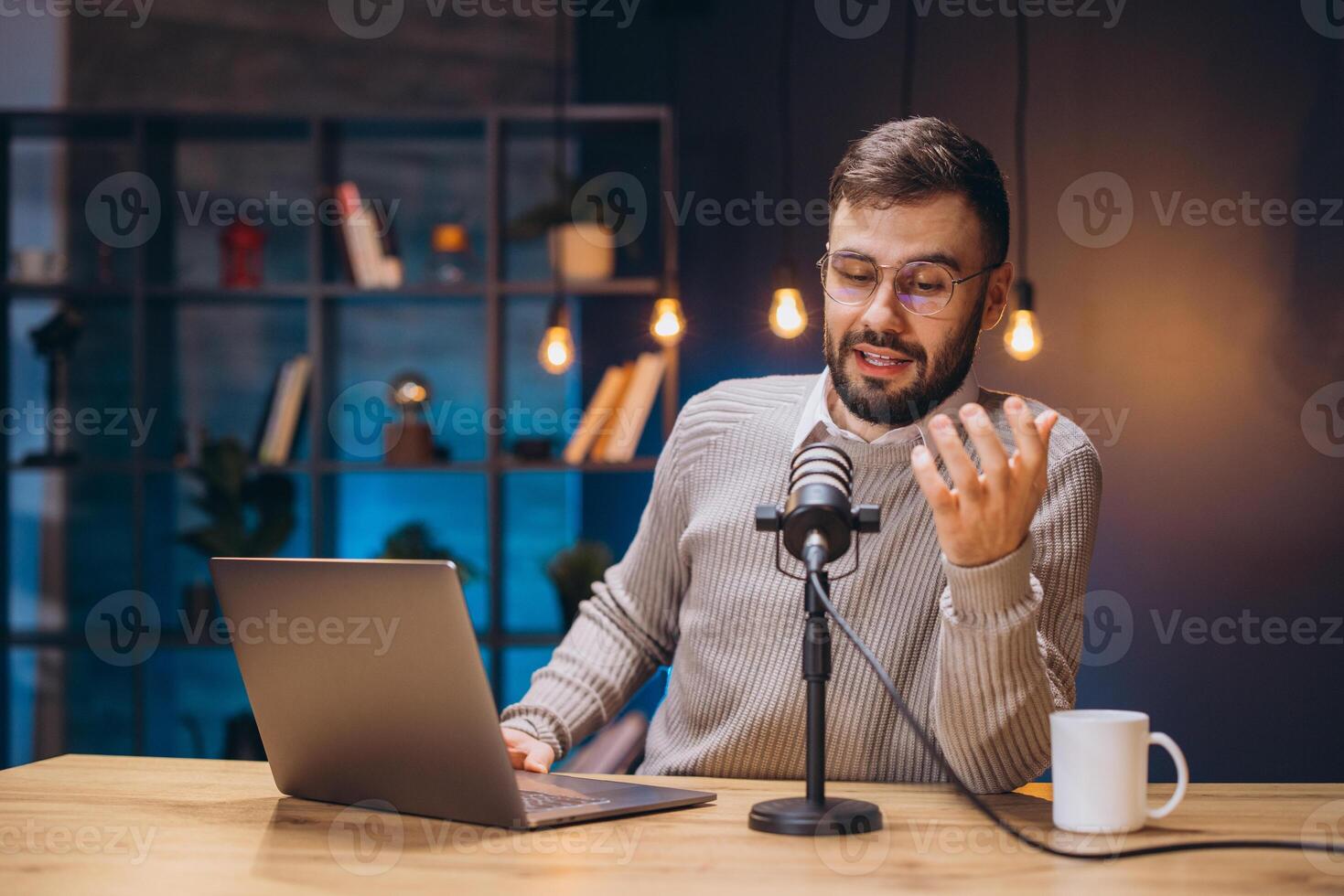 Radio host speaking into microphone while working on laptop during podcast recording session photo