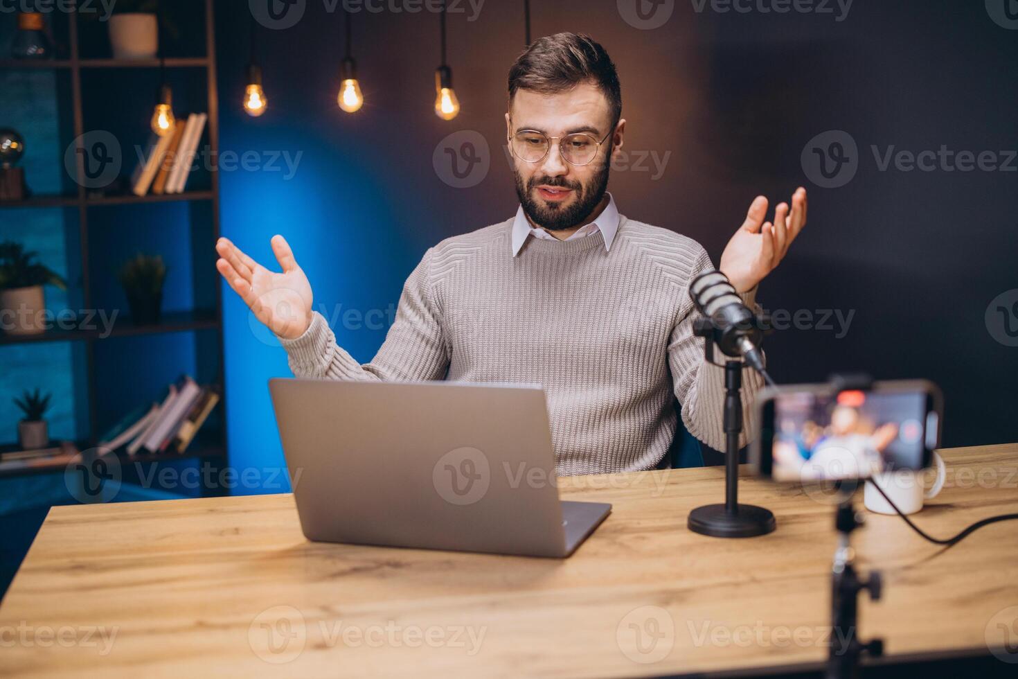 Podcaster working at home studio, speaking into microphone, laptop and smartphone nearby, using hands while talking photo