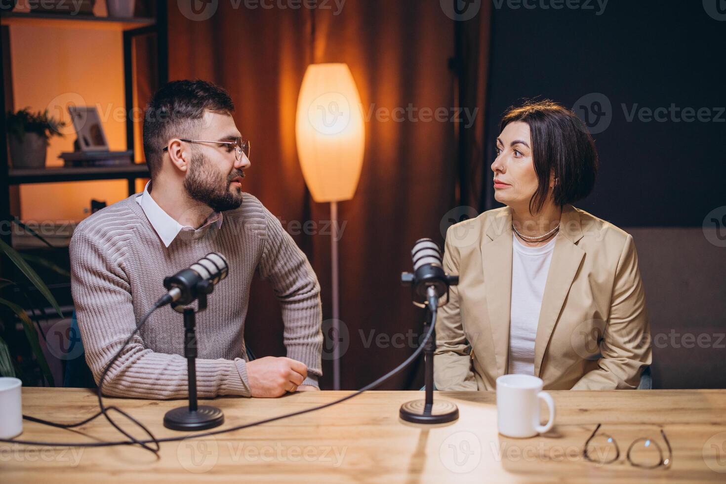 Podcast hosts collaborating, speaking into microphones inside modern recording studio photo