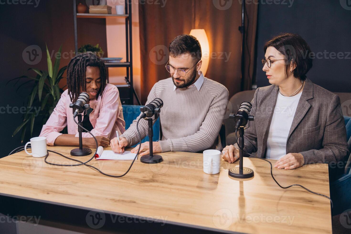 Content creators recording audio in a studio with microphones and equipment, discussing and taking notes for their podcast photo