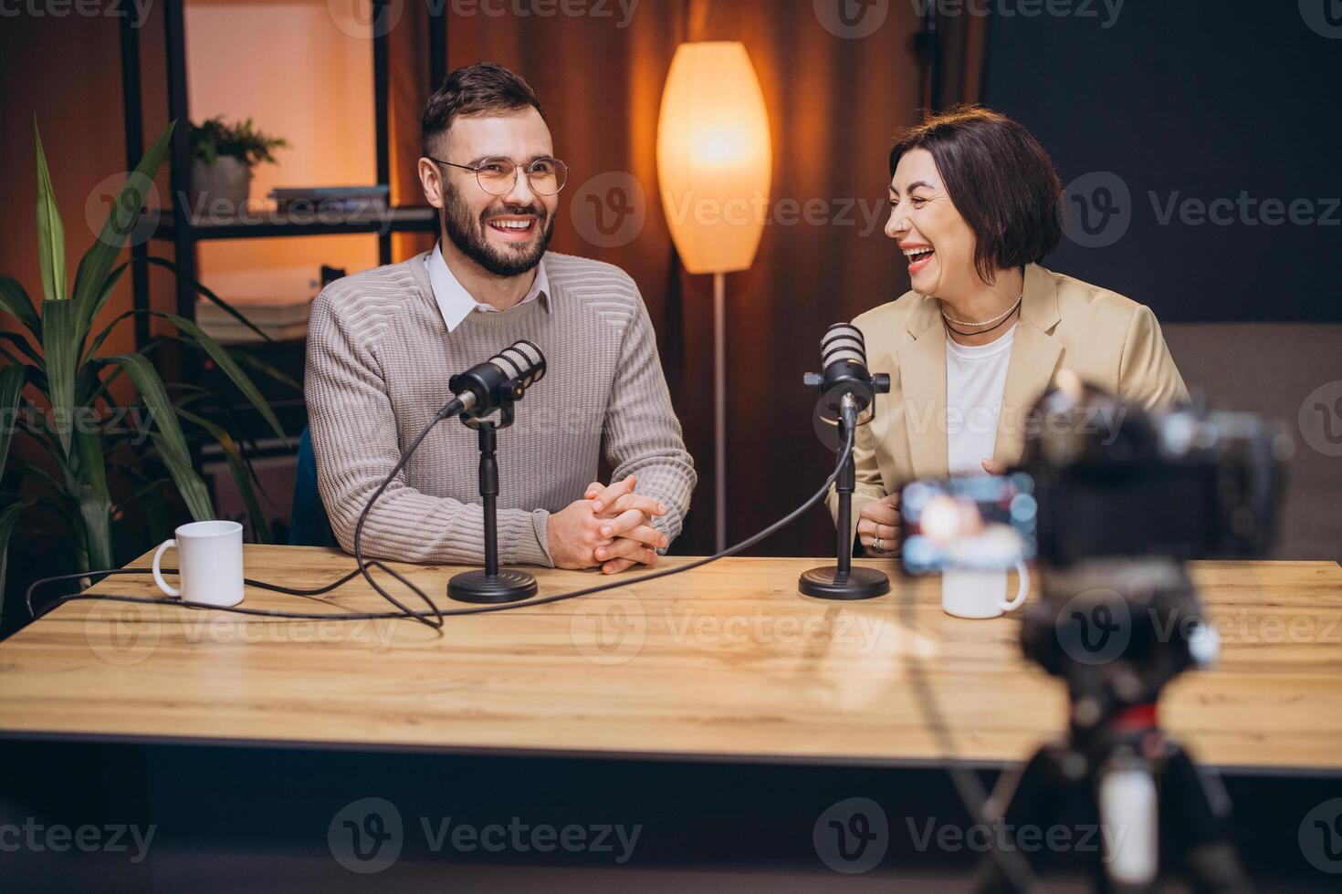 Cheerful podcast hosts laughing while recording inside sleek, contemporary studio, highlighting collaborative creative energy photo