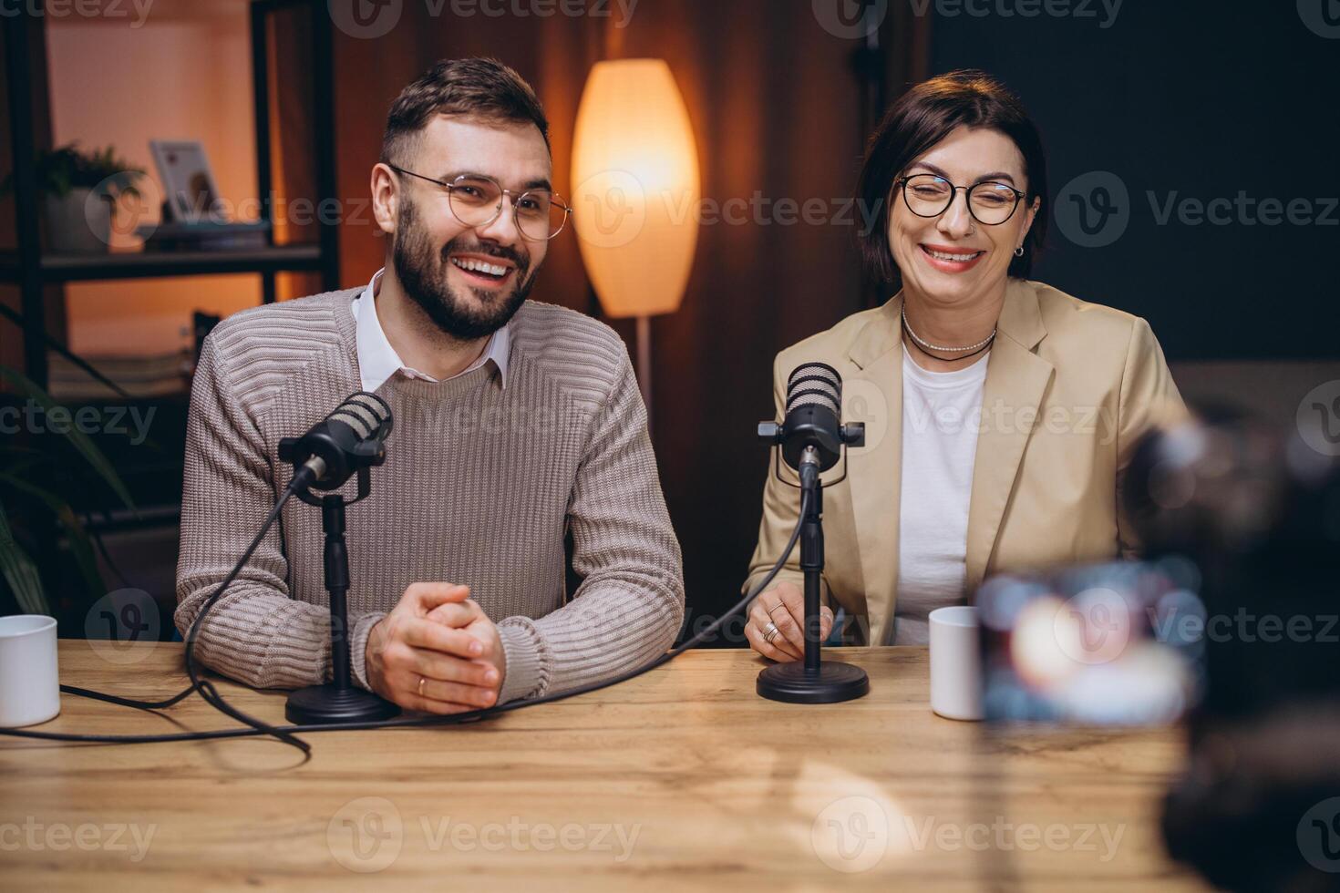 Two happy podcasters, a man and a woman, are recording a new podcast episode in a professional studio photo