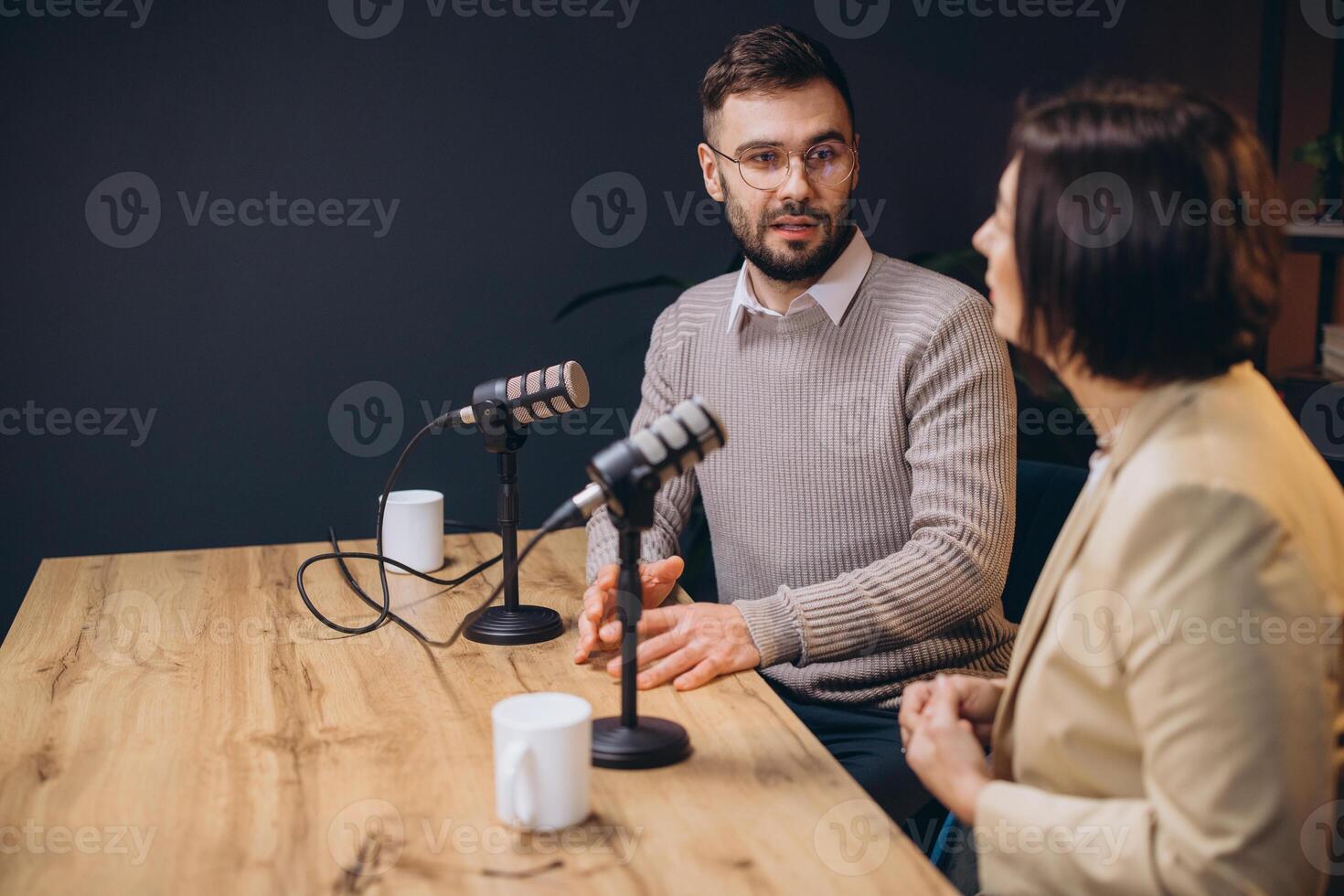 Podcasters discussing topics animatedly, sitting at sleek microphones inside contemporary recording studio with sound absorbing walls photo