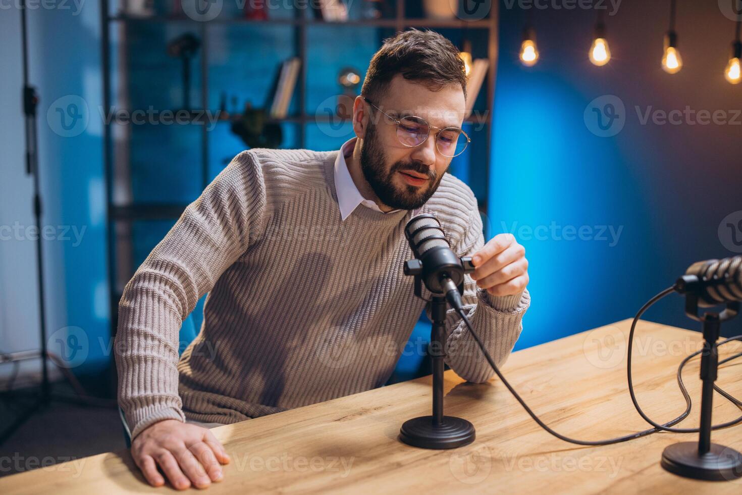 Young man recording a podcast in a professional home studio, speaking into a microphone and adjusting settings photo