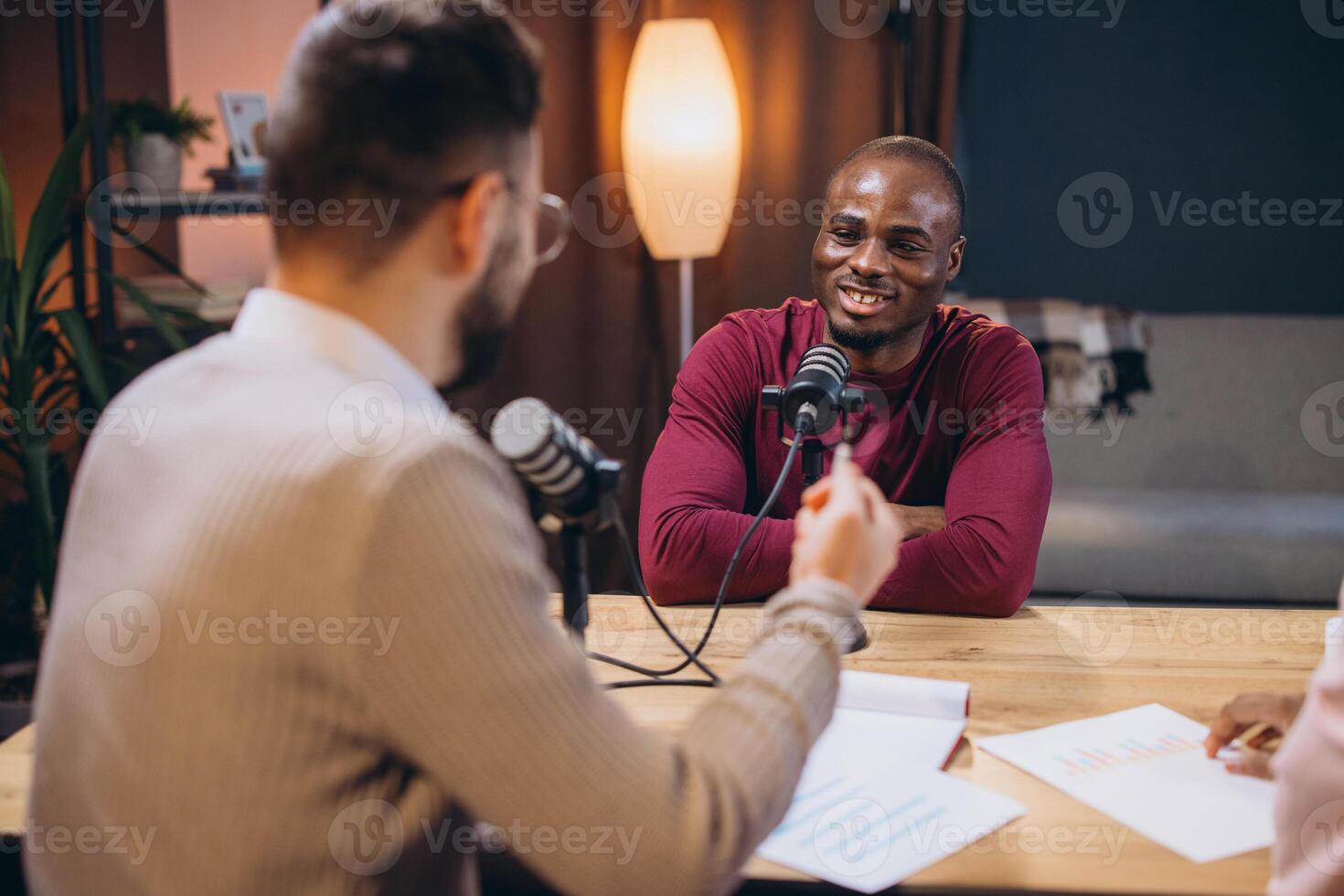 Podcasters recording dialogue, leaning toward microphones in professional sound studio, collaborating on audio content creation photo