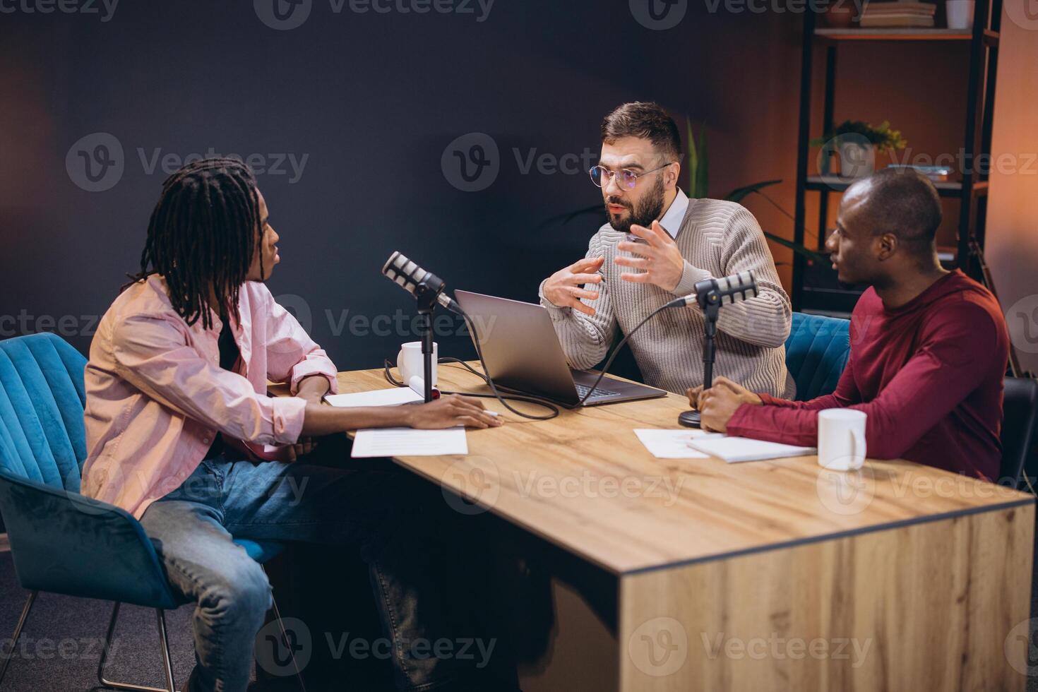 Podcasters discussing animatedly while recording in professional studio, surrounded by microphones, sound boards, and high tech recording gear photo