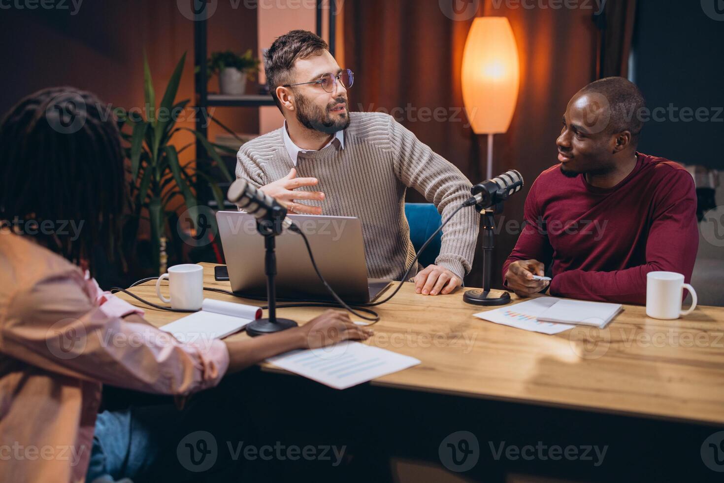 Three podcasters discussing a new topic in a professional home studio, using microphones and laptop photo