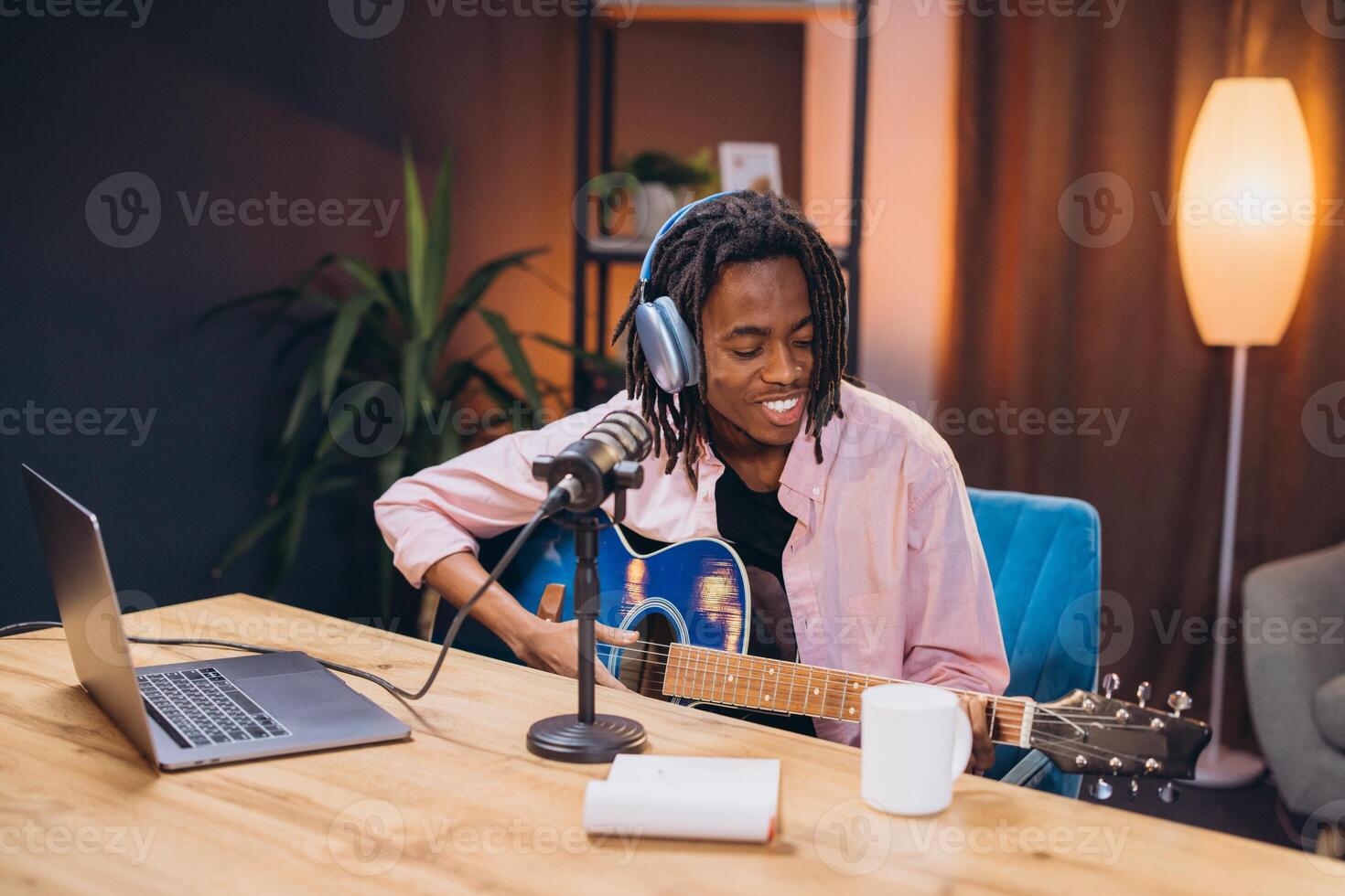 African American mane musician recording podcast, working at home studio with guitar, microphone, laptop in modern workspace setting photo