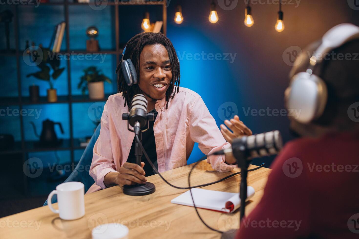 Two young podcasters wearing headphones and speaking into microphones while recording a podcast episode in a studio photo