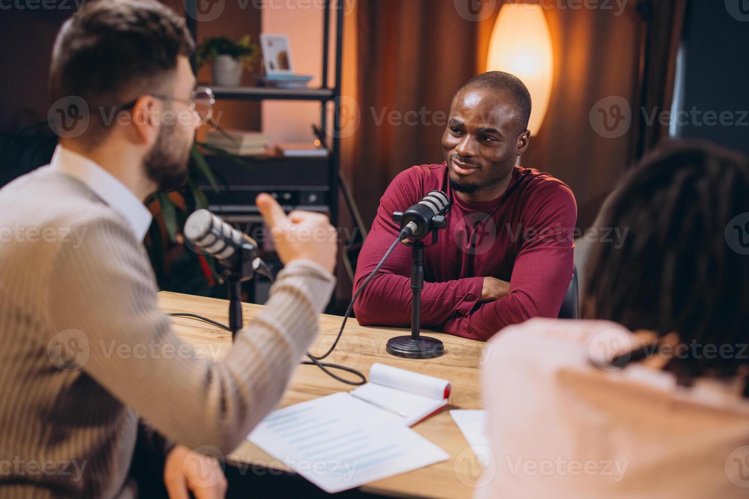 Podcasters collaborating during live recording, speaking into microphones within sleek professional studio environment photo