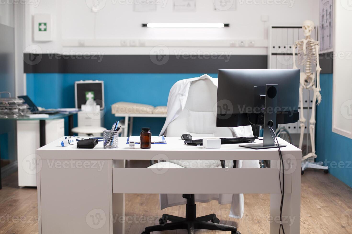 Bright doctors office with sleek furniture and no people present highlighting clean and organized workspace. White desk holds computer and medical documents ready for next healthcare consultation. photo
