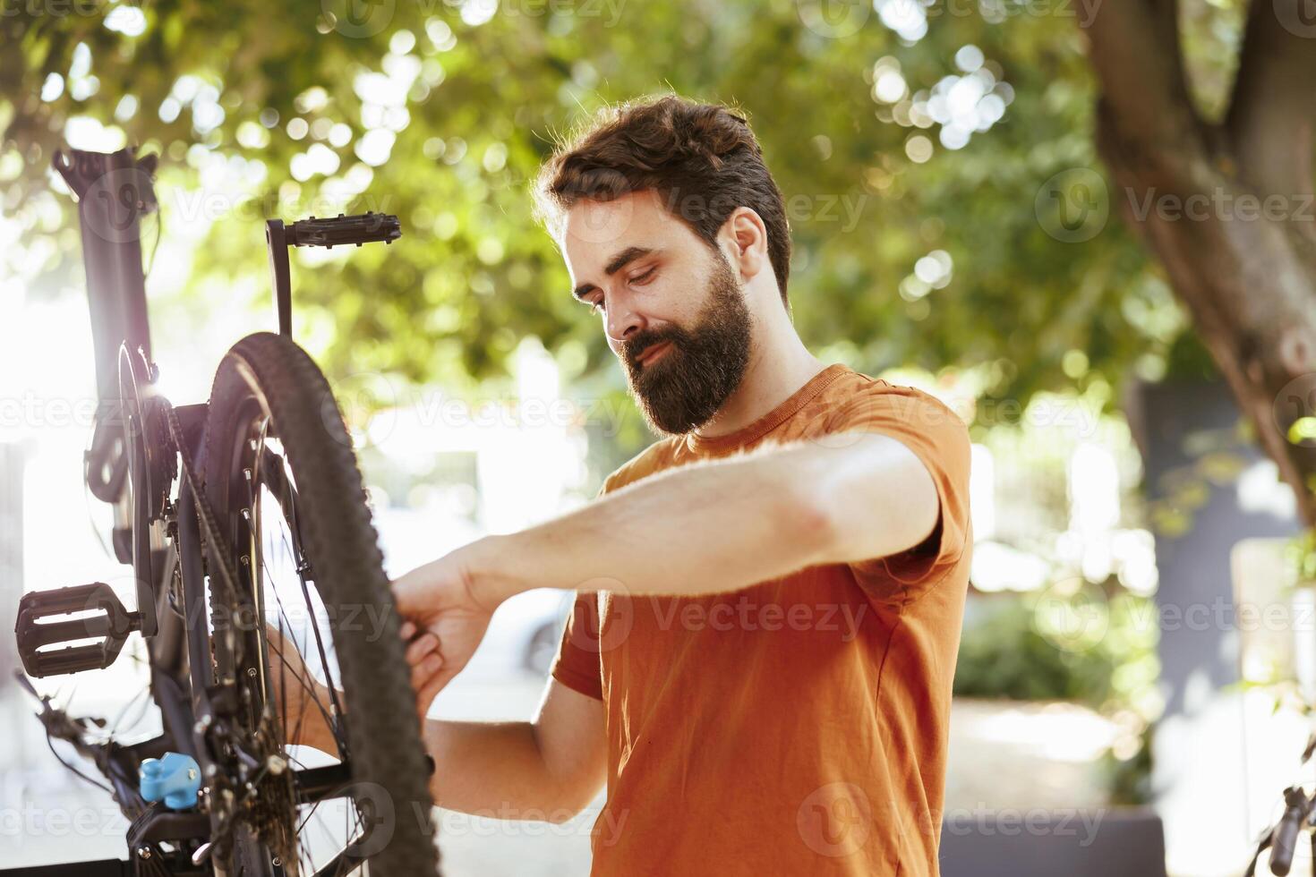 Young healthy caucasian man fixes his own bicycle in the backyard while performing yearly maintenance on outdoor vehicles with the use of professional tools. Bike pedal service and repair as summertime hobby. photo