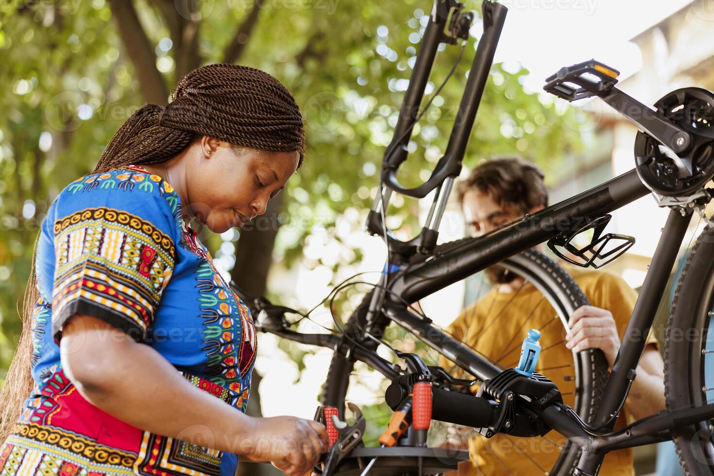 Sporty black woman and caucasian man servicing and adjusting bike components with expert work tools for annual summer maintenance. Healthy multiracial couple examining toolkit and repairing bicycle. photo