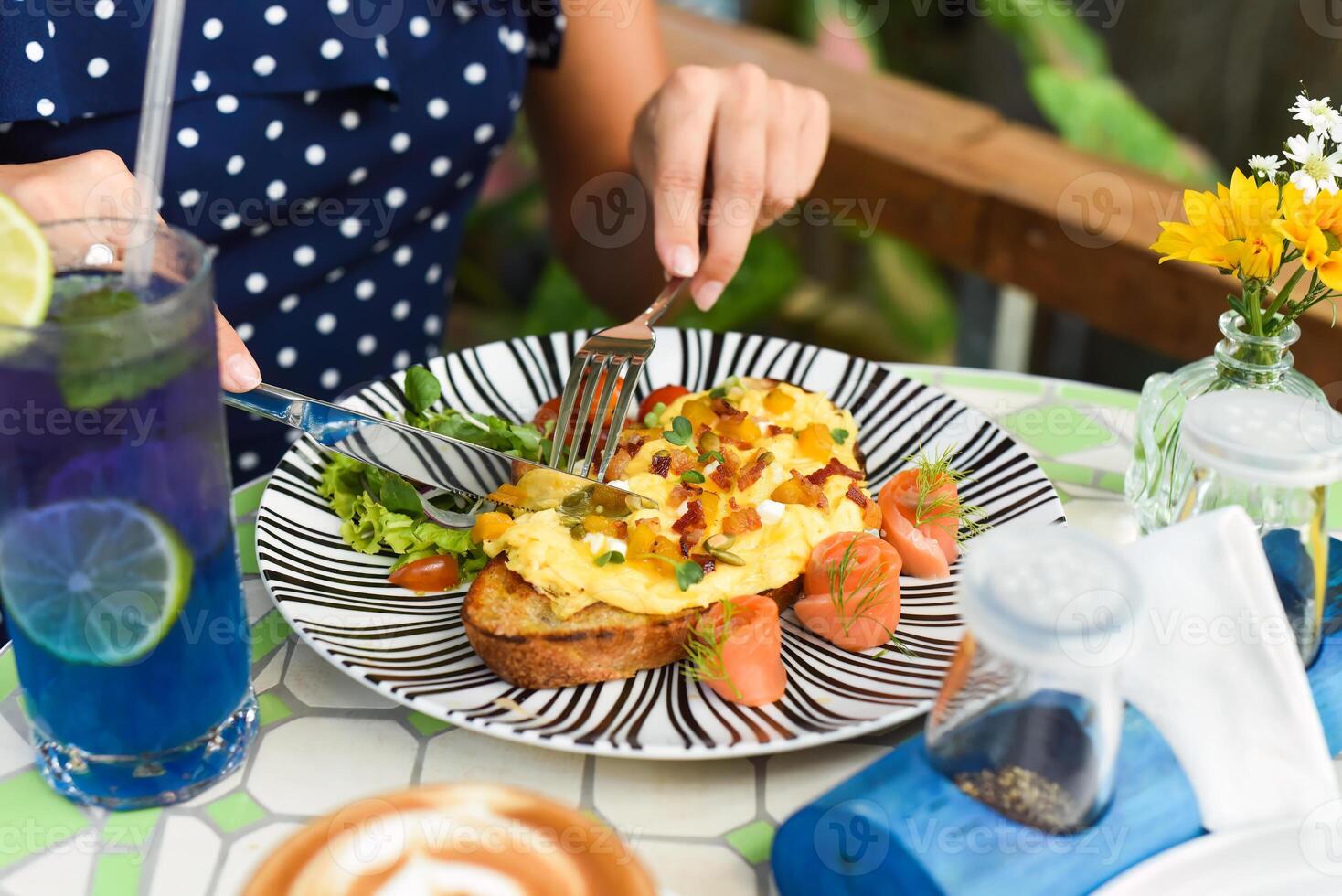 Woman holding knife and fork cutting toast with scrambled eggs pumpkin puree and cubes, smoked salmon and pumpkin seeds photo