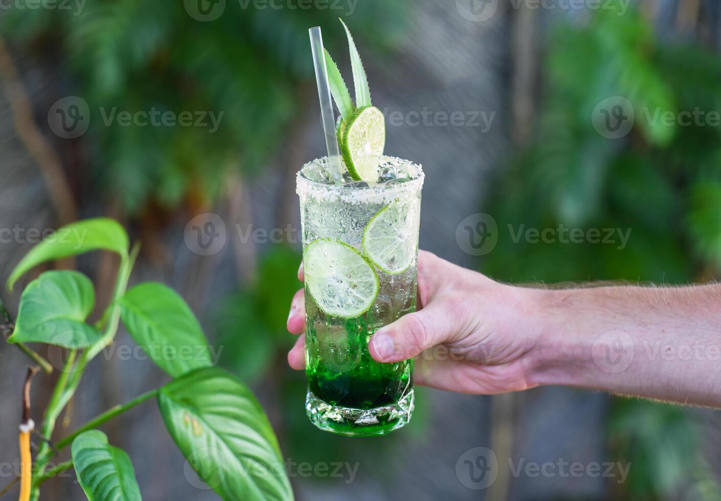 male Hand holding panda leaves lemonade with desiccated coconut and green syrup on natural leaves background with copy space photo