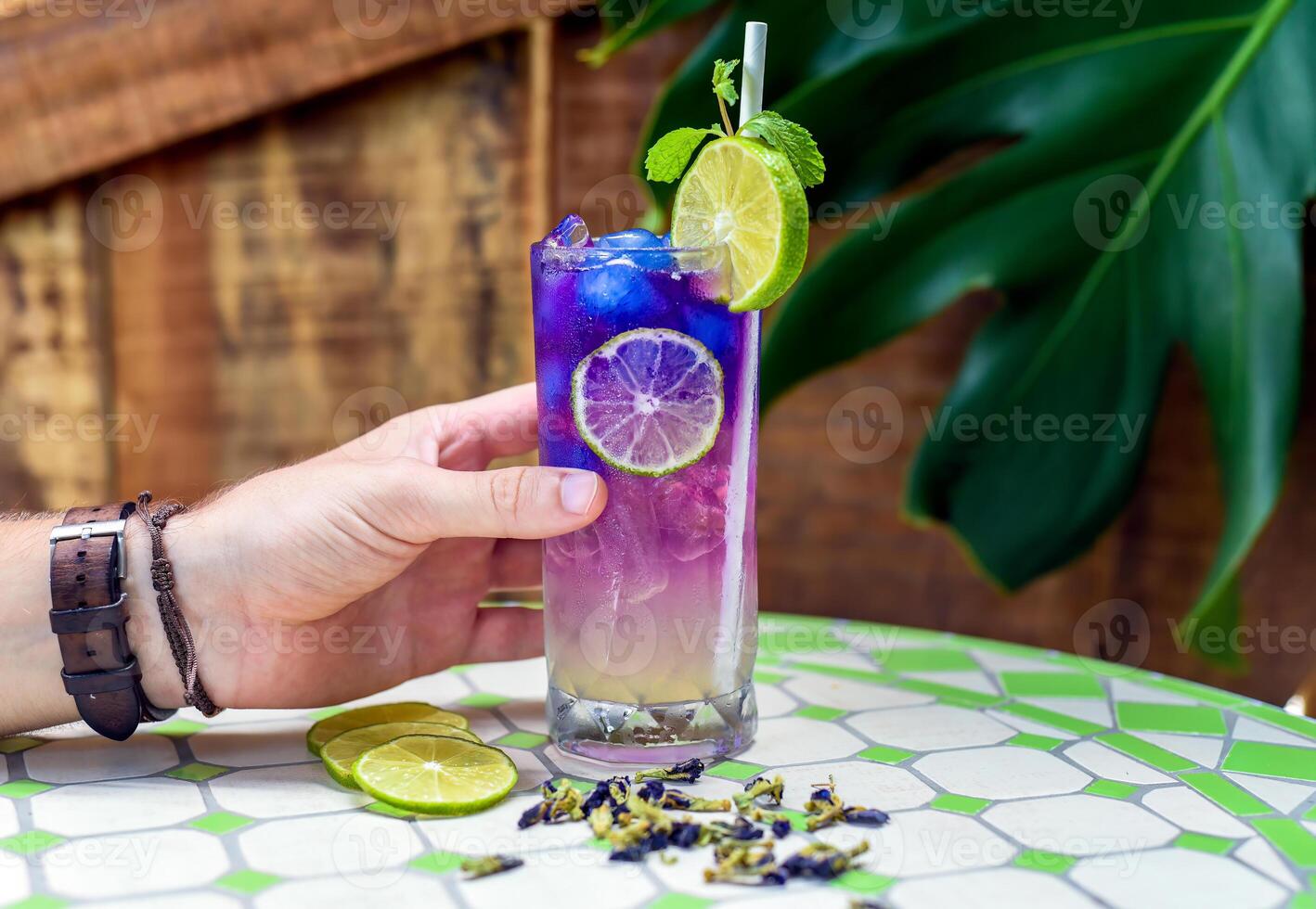 Hand holding lemonade with butterfly pea flowers and blue syrup on narutral leaves background with copy space photo