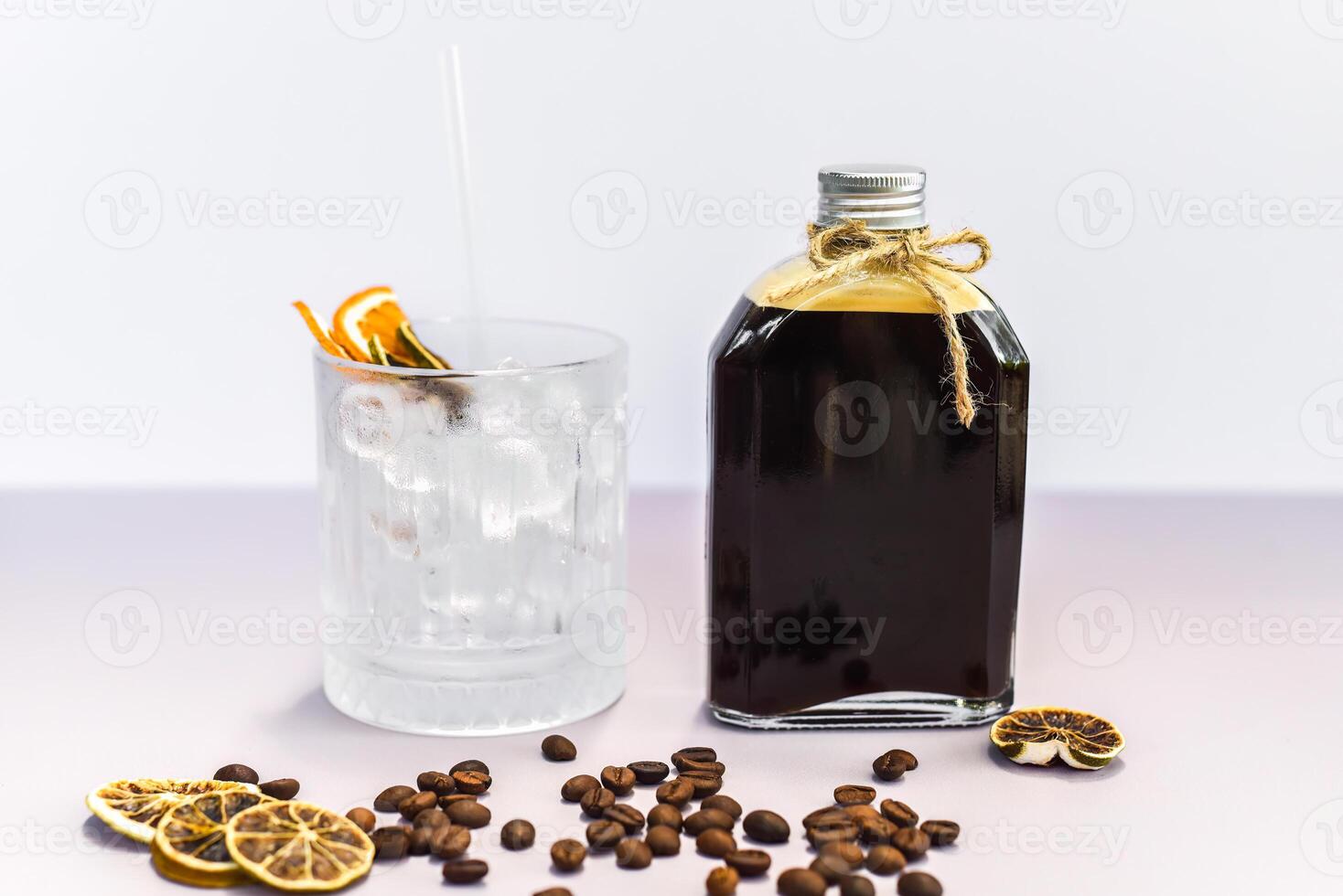 Cold brew coffee in a bottle with transparent glass full of ice on light gray background side view photo