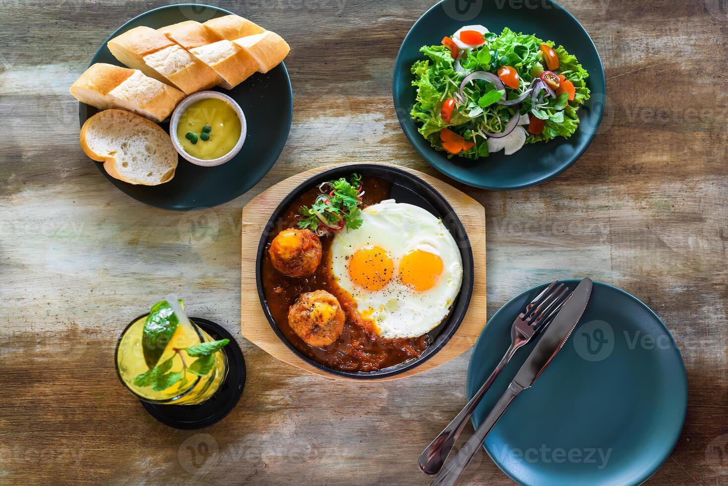Vietnamese Banh mi chao with salted eggs yolk meatballs, tomatoes relish, fried eggs and served with sauce, salad and lemonade drink photo