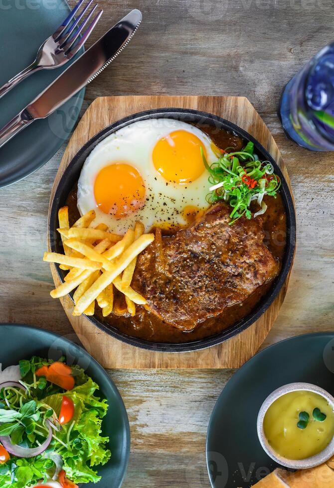 Vietnamese steak with french fries, fried eggs, baguette, served with lemonade drink, vegetable salad photo