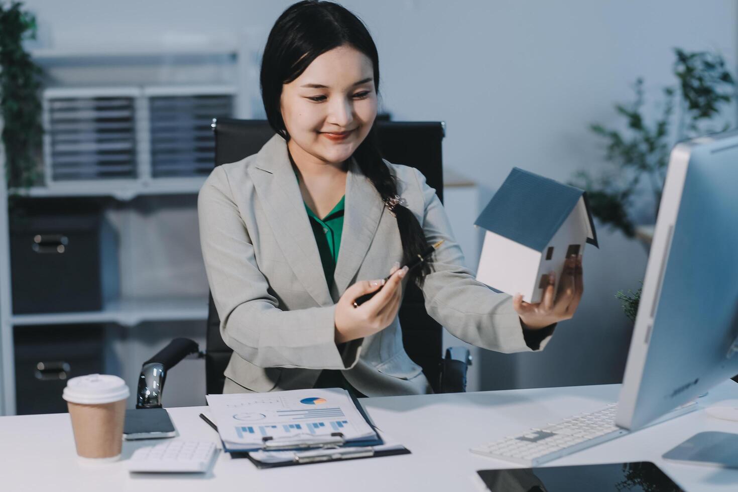 Asian businesswoman holding house model and looking at computer screen photo