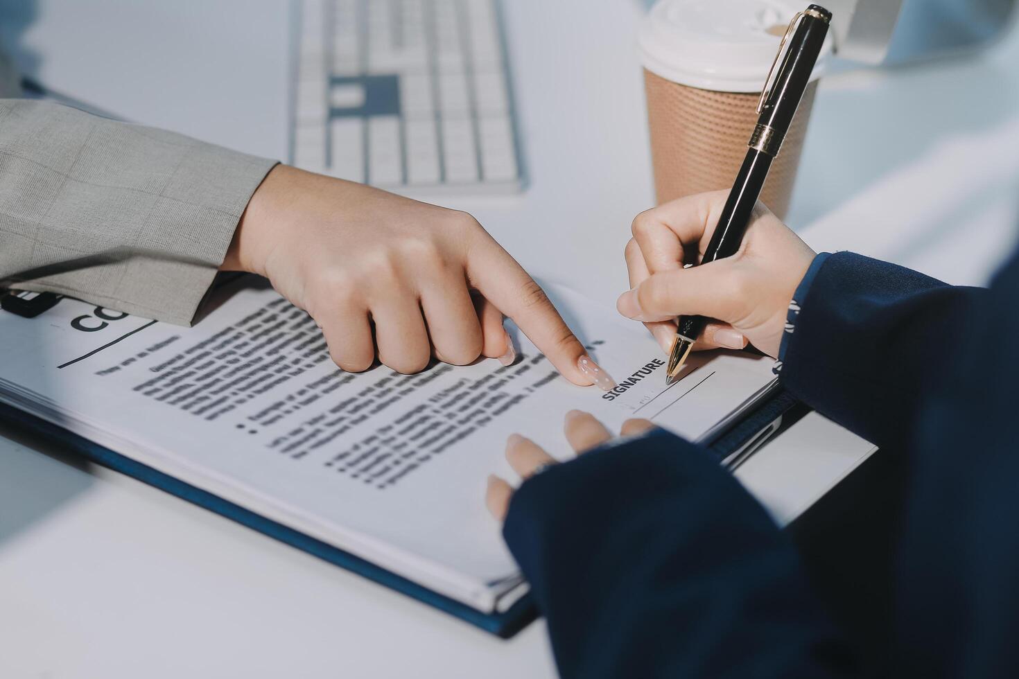 Two people are signing a document on a desk photo