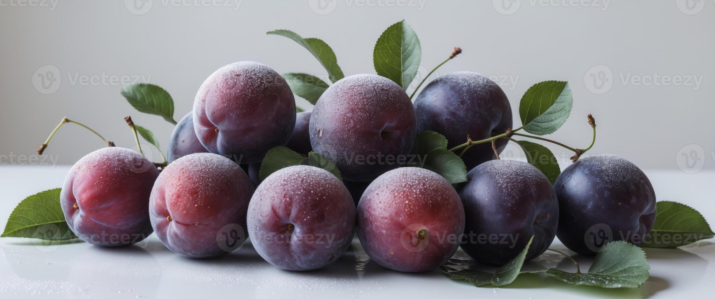A cluster of fresh plums accompanied by lush green leaves sit on a clean white surface photo