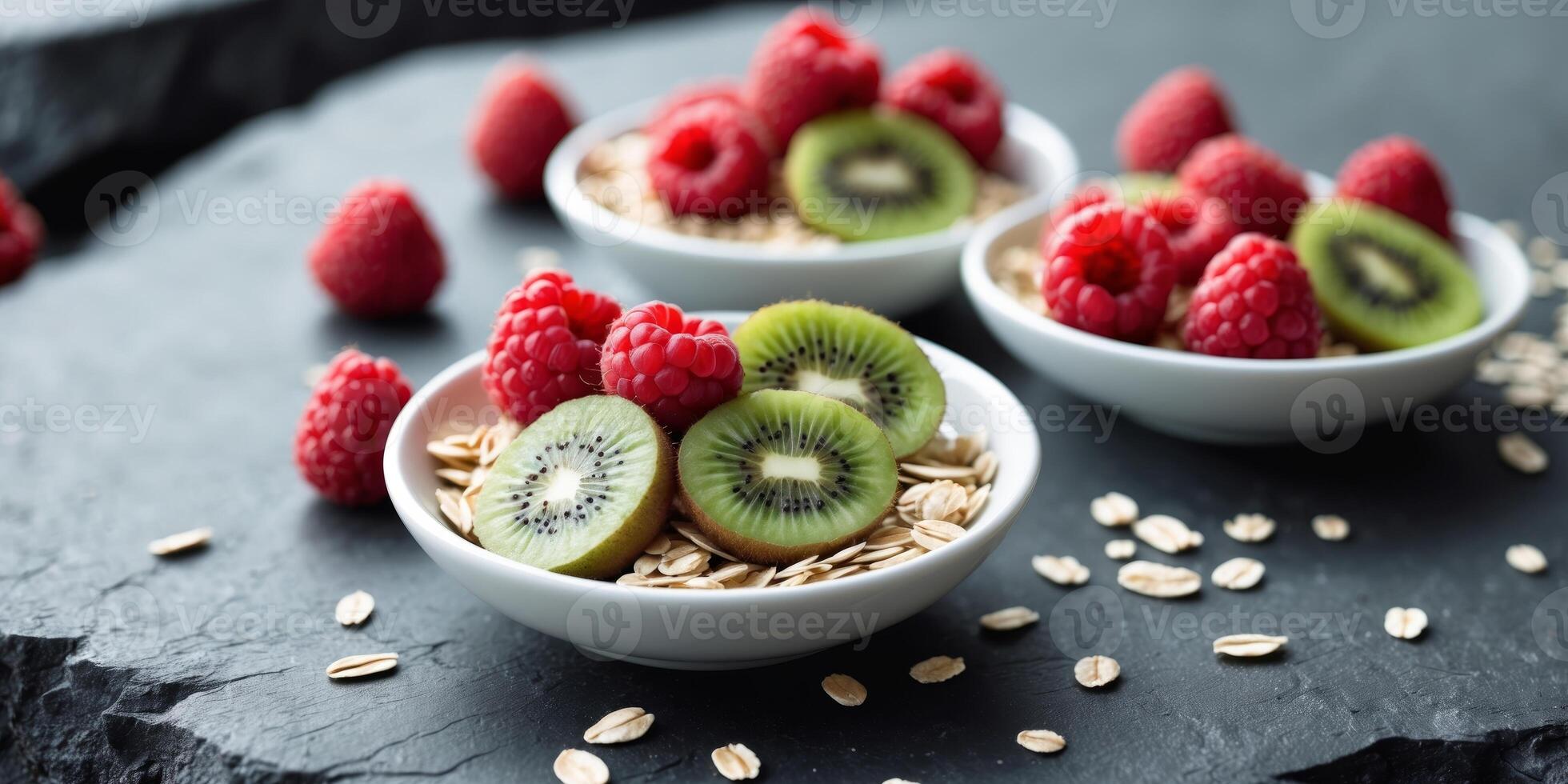 Fresh raspberries and kiwi slices in bowls with oats scattered on dark stone surface Copy Space photo
