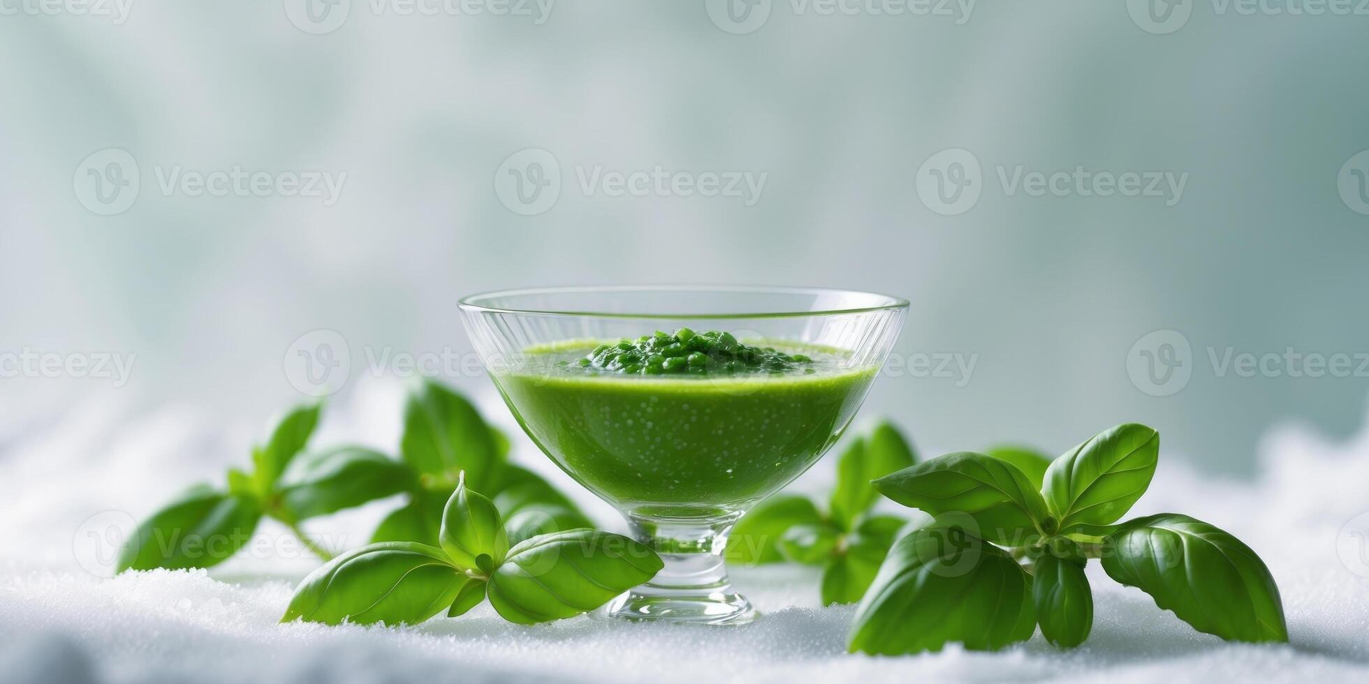 Bowl of green sauce surrounded by fresh basil leaves on white surface with Copy Space photo