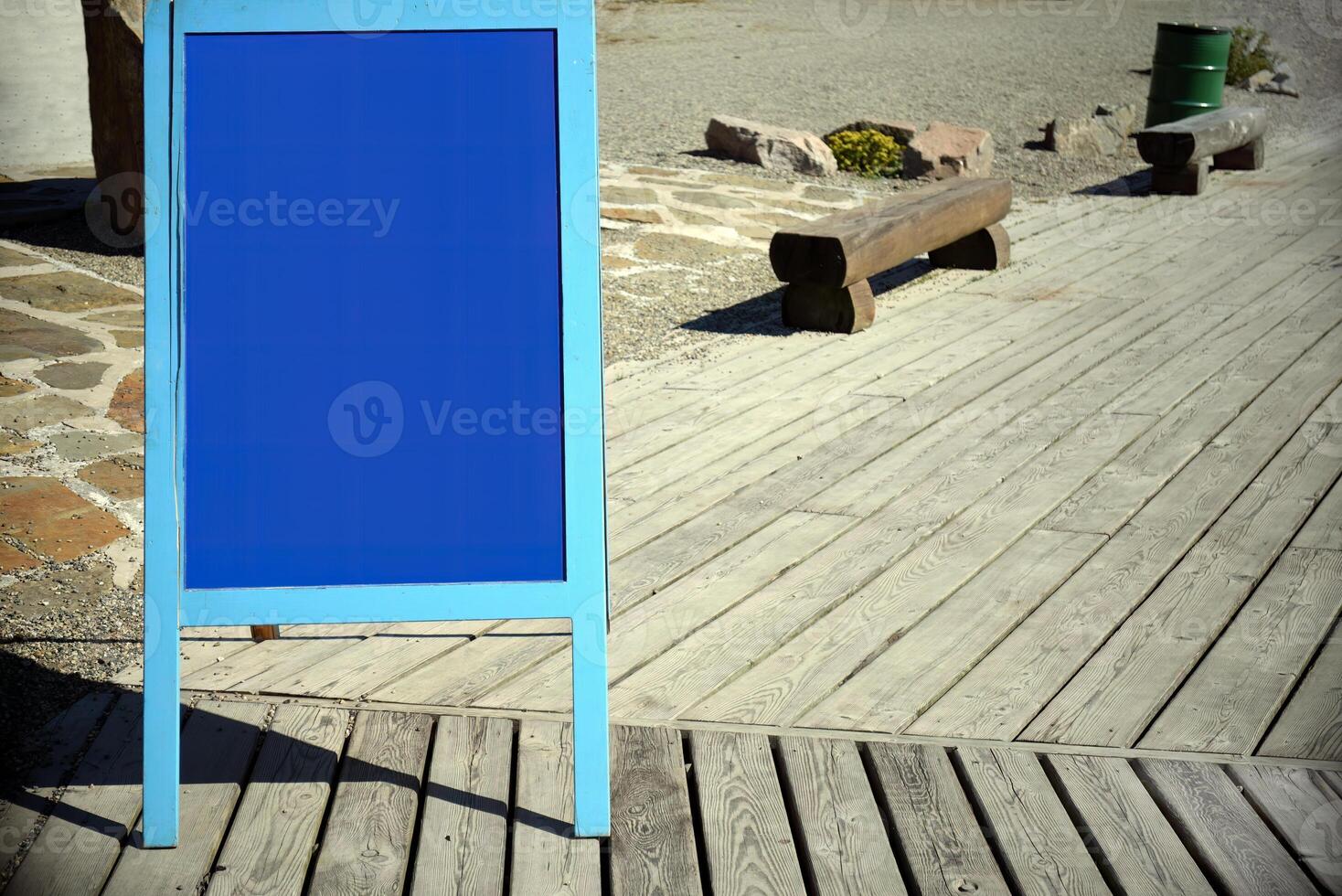 Blue blank advertising board on city street against wooden path with benches near cafe. photo