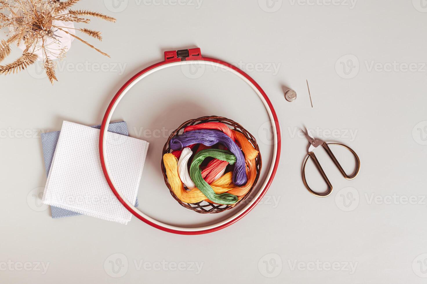 Basket with colored floss, canvas, embroidery hoop and scissors on gray background top view photo