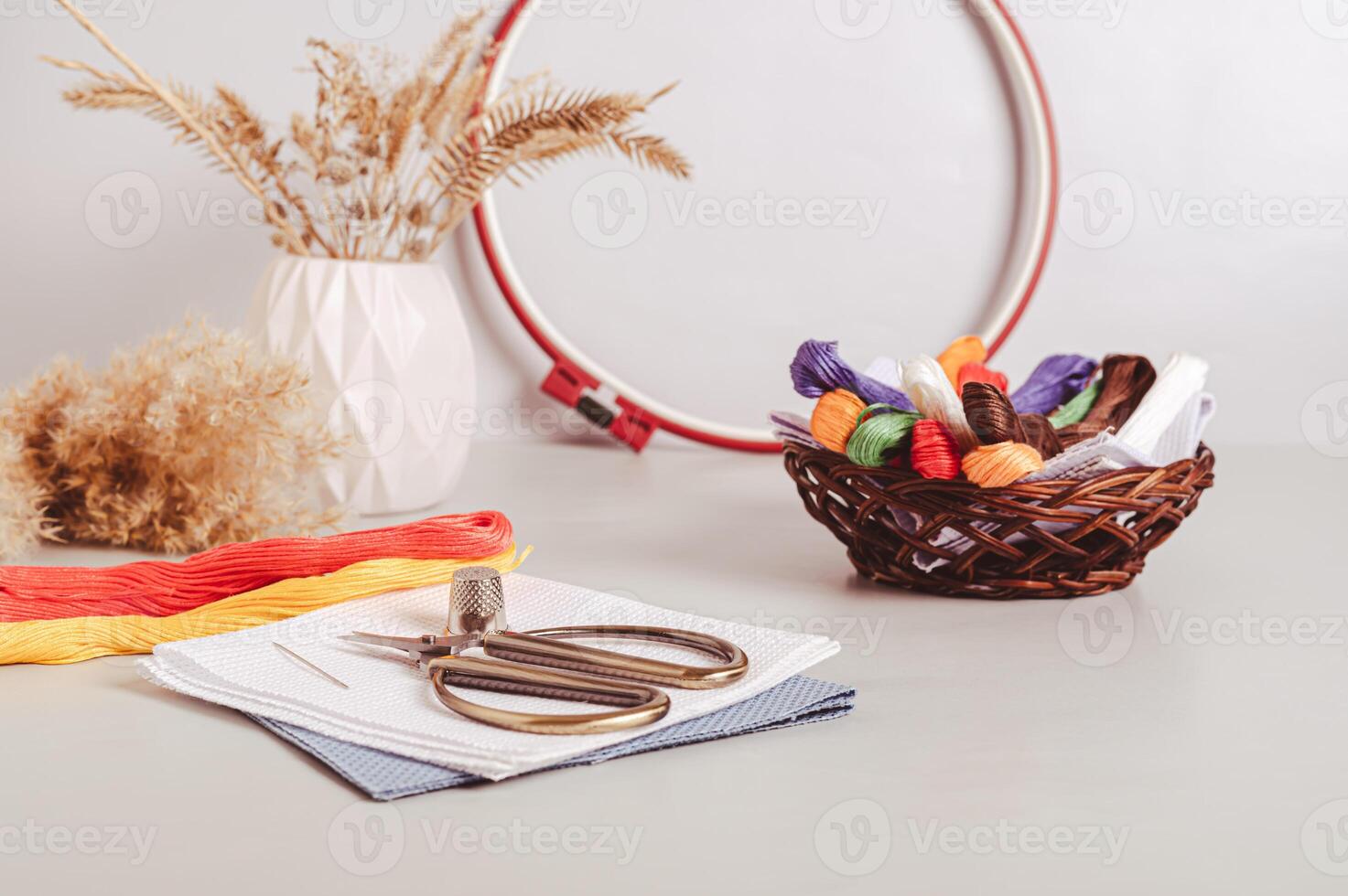 Canvas, embroidery floss, scissors, needle, thimble and cross stitch hoop on table photo