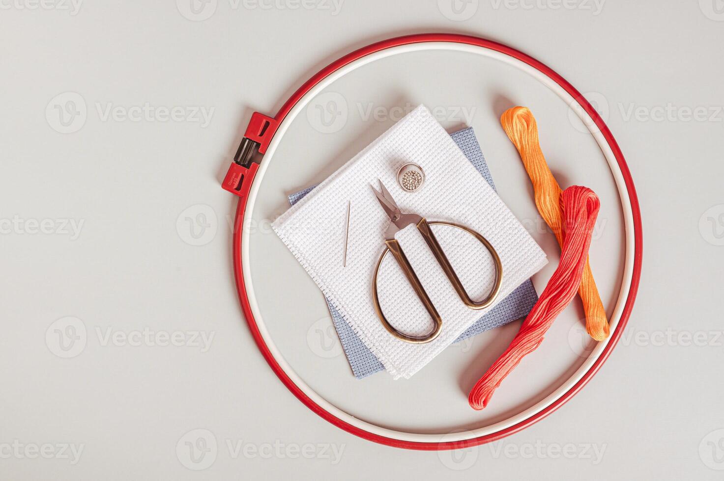 Close up of anvas, embroidery floss, scissors, needle, thimble and cross stitch hoop top view photo