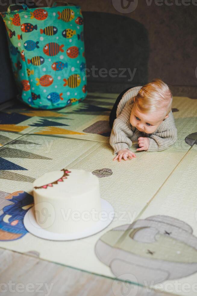A blond baby crawls on the floor at home and wants to eat a sweet cake. Child development. A boy learns to crawl. photo
