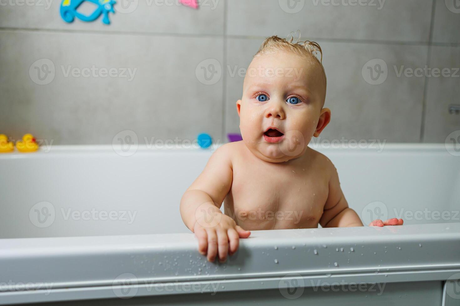 A blue-eyed baby with a bare torso is standing in the bathroom and smiling. Emotions of joy in a baby. Baby's personal hygiene. photo