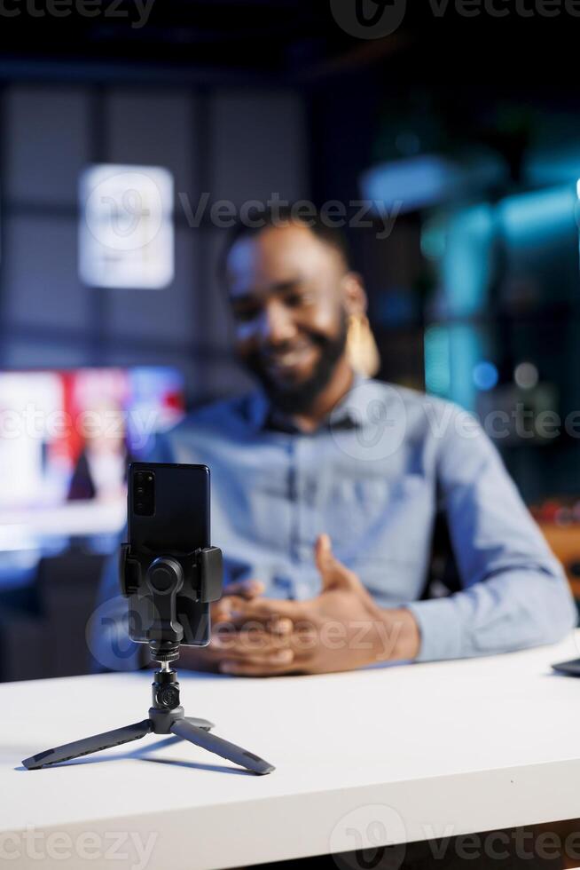 Influencer in blurry background using cellphone to film vlog channel intro for online streaming platforms. Viral media star greets fanbase, presenting today topic, recording with phone photo