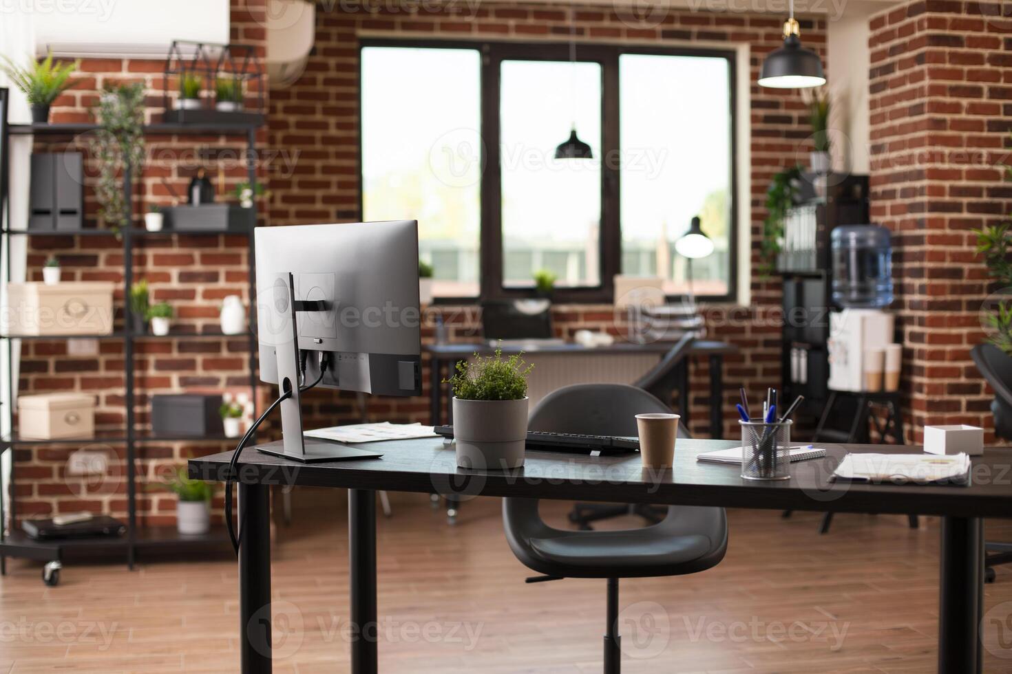 This empty, well arranged workspace has modern desk, desktop monitor, and financial documents. Vacant brick wall room is ready for business projects and marketing strategy development. photo