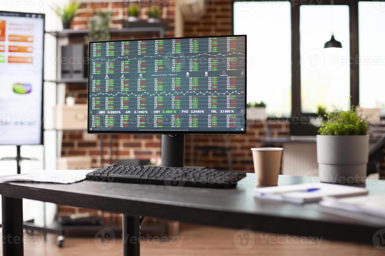 Vacant modern workspace with desktop pc displaying company statistics, financial graphs, and trading tools. Organized office supplies and plant decoration creates professional setup. photo