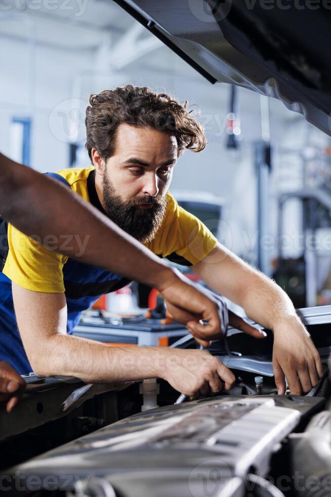 Trained repairmen in auto repair shop working together on fixing car, discussing best options. Teamworking colleagues collaborating on servicing broken vehicle, checking for faulty motor photo