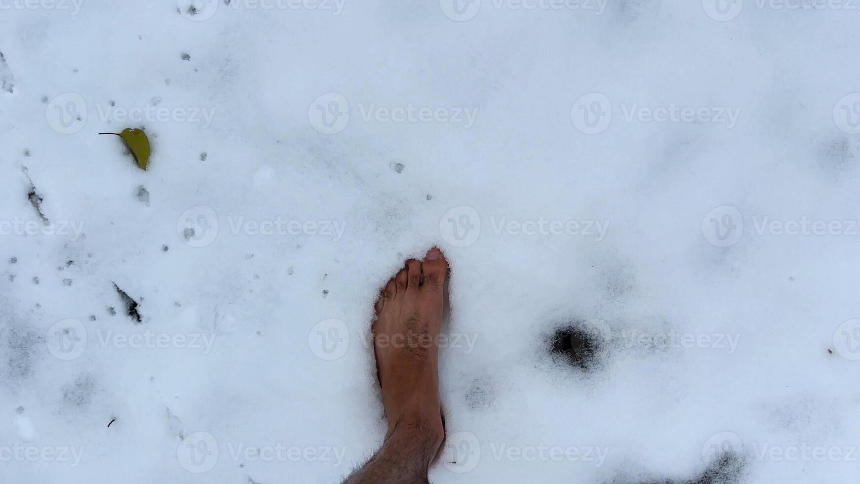 Top view of male bare feet stepping on white snow. Legs of man going on snowy trail. Young guy hardening at cold winter. Concept of healthy lifestyle. POV Slow motion photo